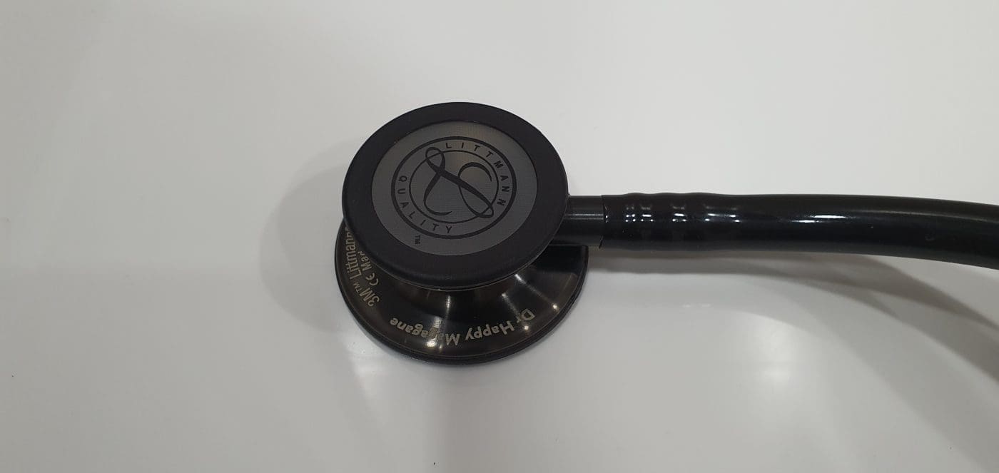 Black-finish Littmann stethoscope chestpiece with an engraved name, lying on a white surface